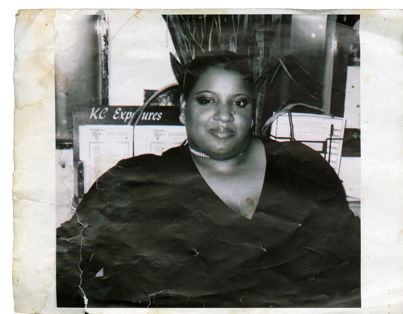 Big Beauty poses in front of KC Exposures publications. The photo is in black and white. 