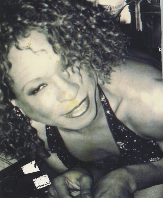 Tisha Taylor smiles in a close-up photo. She is wearing a sparkly top with a plunging neckline. 